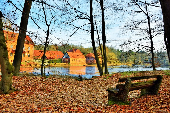 Die historische Ahauser Backsteinmühle hinter dem Mühlenteich in der Herbstsonne, davor eine Bank im Herbstlaub