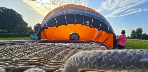 Hinter dem Korb, der gekippt auf dem Boden liegt, wird der orangefarbene Ballon mit heißer Luft gefüllt und bläst sich dadurch auf