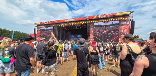 Die Bühne des Hurricane Festivals ist mit hellen Lichtern beleuchtet, während Fans in schwarzen T-Shirts und bunten Outfits tanzen.