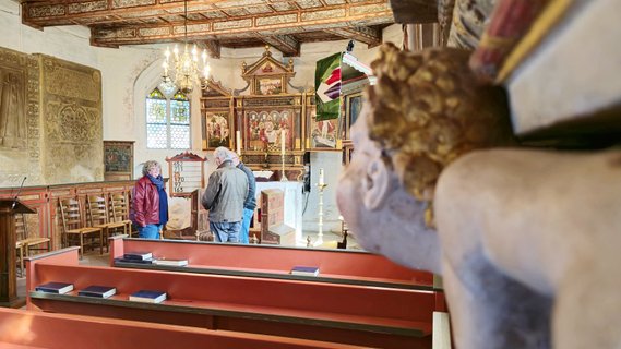 Ein Engel in der Unschärfe und Personen bei einer Führung in der Schärfe in der Oeser Kirche