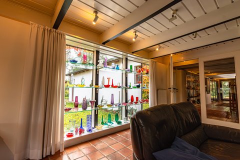 Glasvitrine mit bunten Vasen und Flaschen an einer Fensterfront im Haus Kreienhoop