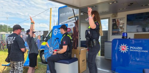 Zwei Polizisten stehen an einem Informationsstand, während Festivalbesucher an einem Glücksrad teilnehmen.