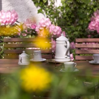 Kaffeegedeck mit Porzellan-Kaffeekanne zwischen gelben und rosafarbenen Blumen