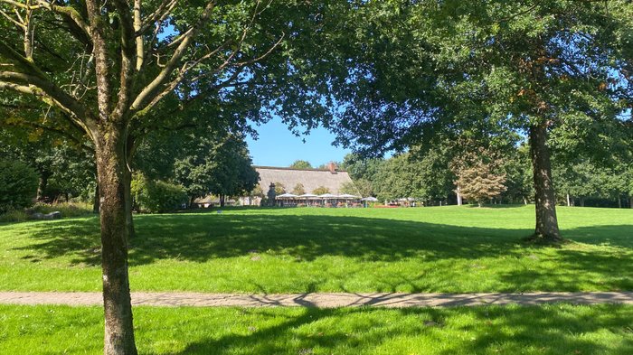 Hinter einer großen grünen Wiese ist das historische Fachwerk-Haus am See in Bremervörde klein zu sehen