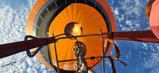 Blick von unten in den Ballon mit der Flamme, darüber ist strahlend blauer Himmel mit kleinen Wolken zu sehen