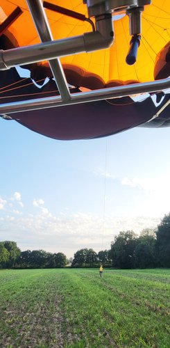 Udo steht klein im Hintergrund auf dem Landefeld und hält den Ballon am Seil, der oben im Bild zu sehen ist