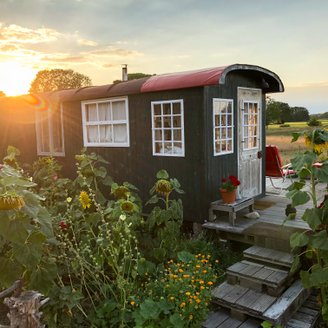 Ein alter Bauwagen, in dem übernachtet werden kann, vor einem Sonnenuntergang an einer Wiese