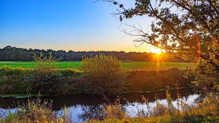 Abendstimmung beim Sonnenuntergang an der Oste mit weitem grünen Feld hinter dem Fluss