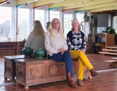 Die Gästeführerinnen Alinda und Irmela sitzen auf einer Holztruhe vor Spiegel im Haus Kreienhoop