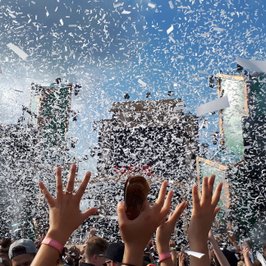 Besucher strecken die Hände hoch im Konfittiregen auf dem Elektropop-Festival Ferdinands Feld