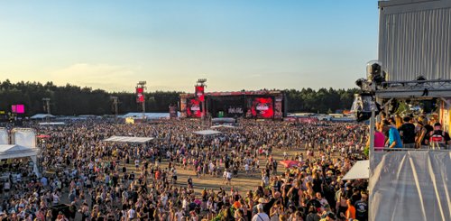 Im Hintergrund leuchten die Festivallichter, während die Besucher sich in der offenen Fläche versammeln und die Musik genießen.