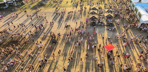 Eine lebhafte Festivalatmosphäre mit Menschenmengen und langen Schatten, die über das Gras ziehen.