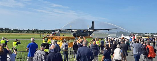 Viele Menschen stehen an einem Sommertag vor der Transall, die feierlich bei ihrer Ankunft mit Wasser besprüht wird