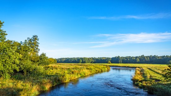 Die Wümme schlängelt sich durch eine flach-weite Wiesenlandschaft, der Himmel strahlt blau