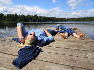 Eine Frau liegt mit ihren Kindern, alle blau gekleidet, entspannt auf dem Steg am Bullensee