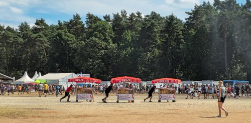 Eine lebhafte Festivalatmosphäre entsteht durch die Menschenmenge und die bunten Essensstände im Hintergrund.