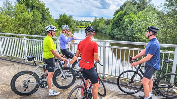 Vier Rennradfahrer machen auf einer Wümme-Brücke eine Pause