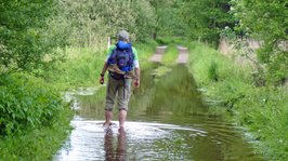 Ein Wanderer läuft ohne Schuhe durch das Hochwasser am NORDPFAD Kirchsteg-Moore-Bäche