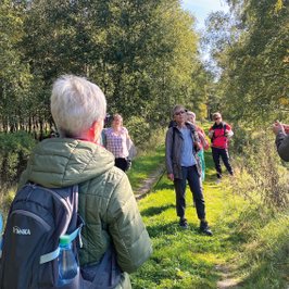 Eine Wandergruppe lauscht der Gästeführerin inmitten einer sattgrünen Natur