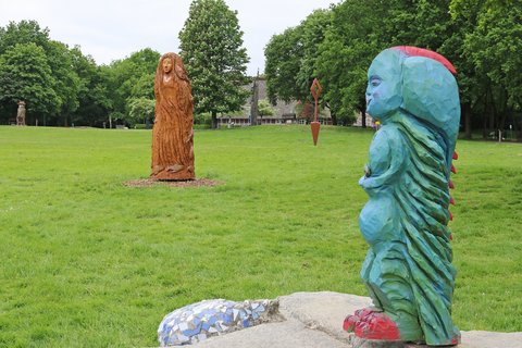 Mehrere Kunstwerke stehen auf einer Wiese am Haus am See, im Vordergrund eine blaue Fantasiegestalt