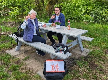 Florian Striebeck und Ingrid auf der neuen von ihr gespendeten Tisch-Bank-Kombination mit einem Glas alkoholfreien Sekt in der Hand