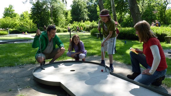 Eine Familie spielt Minigolf, ein Kind plant den letzten Spielzug