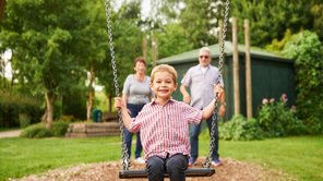 Ein Junge strahlt freudig auf einer Schaukel, hinter ihm stehen die Großeletern