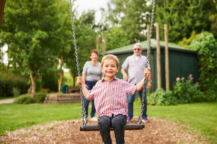 Ein Junge strahlt freudig auf einer Schaukel, hinter ihm stehen die Großeletern