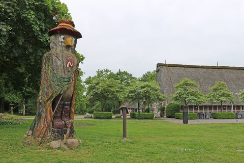 Die Hozzskulptur namens Willy Wandervogel schaut auf die Wiese vor dem Haus am See